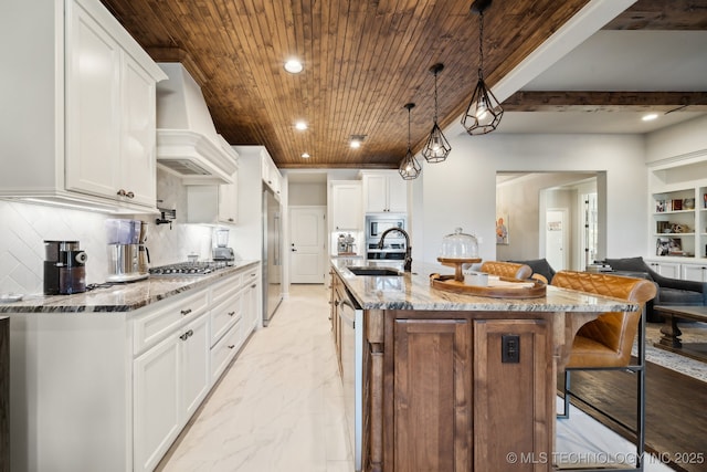 kitchen with a center island with sink, custom exhaust hood, decorative backsplash, and sink