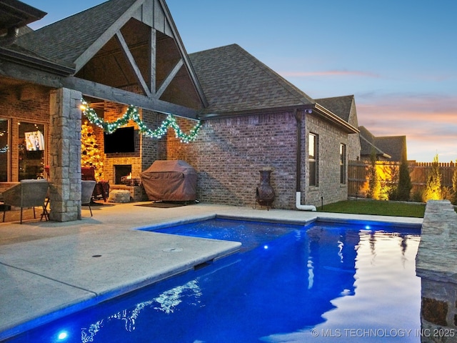 pool at dusk with an outdoor fireplace and a patio area