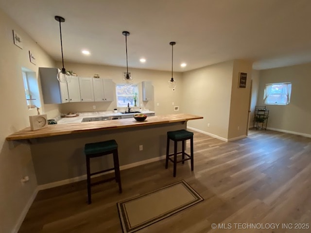 kitchen with a peninsula, dark wood-type flooring, white cabinetry, hanging light fixtures, and a kitchen bar