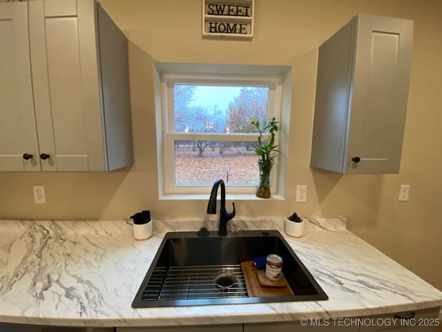 kitchen with light stone countertops, gray cabinets, and sink