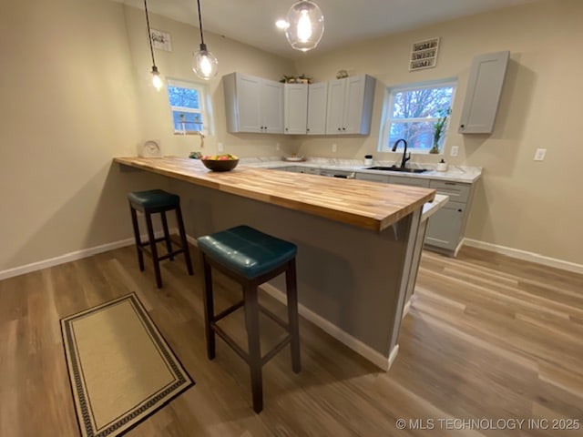 kitchen with sink, wood counters, kitchen peninsula, decorative light fixtures, and a breakfast bar