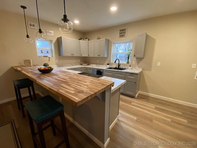 kitchen featuring wood counters, a breakfast bar area, gray cabinets, pendant lighting, and a sink