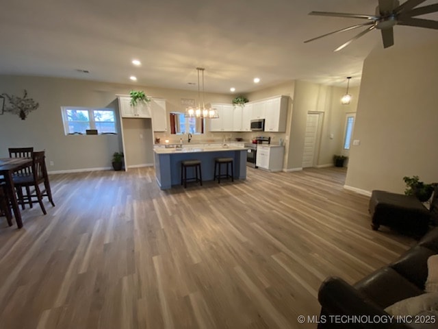 kitchen featuring stainless steel appliances, white cabinets, open floor plan, light countertops, and decorative light fixtures