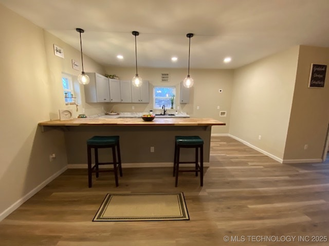 kitchen with kitchen peninsula, dark hardwood / wood-style flooring, a kitchen bar, and decorative light fixtures