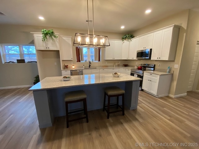 kitchen with sink, light wood-type flooring, appliances with stainless steel finishes, a kitchen island, and white cabinetry