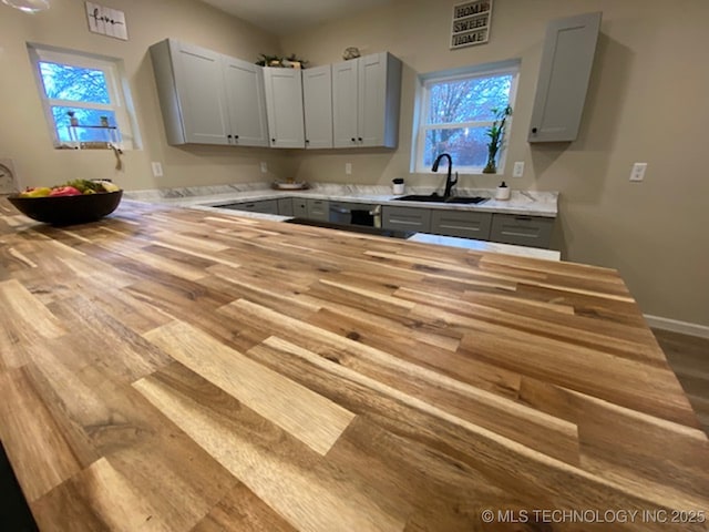 kitchen featuring butcher block counters, light wood-style flooring, gray cabinetry, a sink, and baseboards