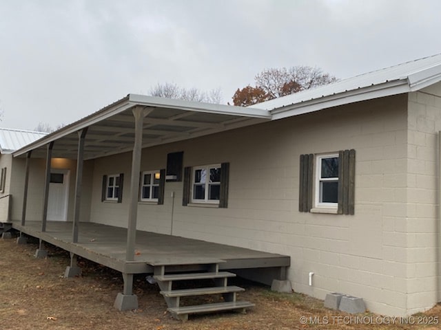 exterior space featuring concrete block siding, metal roof, and a deck