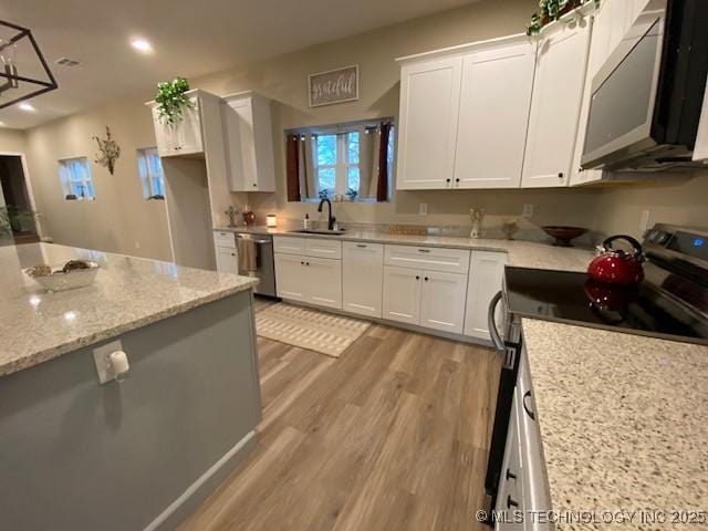 kitchen with light stone counters, stainless steel appliances, a sink, white cabinetry, and light wood-style floors