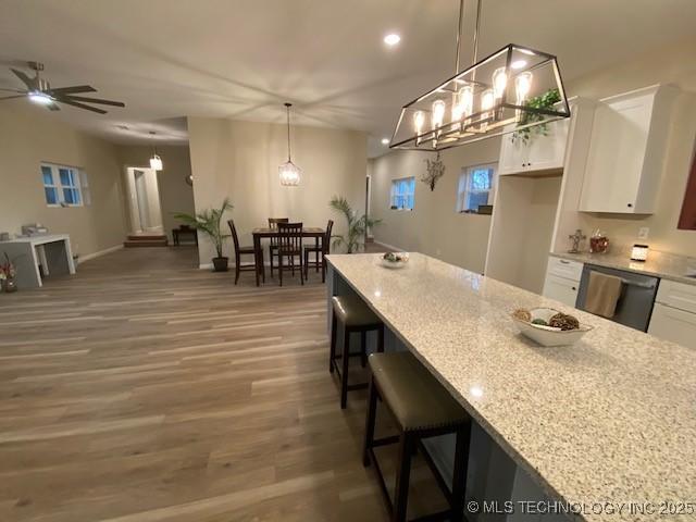 kitchen featuring dishwasher, hanging light fixtures, light stone countertops, white cabinets, and a kitchen bar