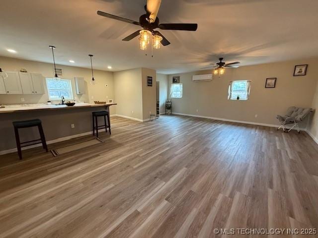 interior space featuring a breakfast bar, light countertops, an AC wall unit, white cabinetry, and open floor plan