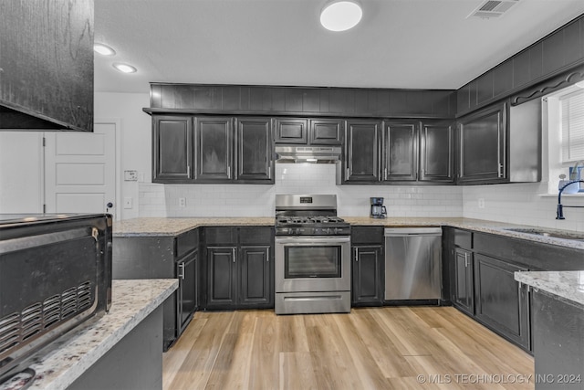 kitchen featuring light wood-type flooring, tasteful backsplash, light stone counters, stainless steel appliances, and sink