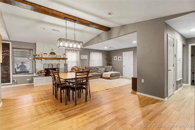 dining room featuring vaulted ceiling with beams, light hardwood / wood-style flooring, and a stone fireplace