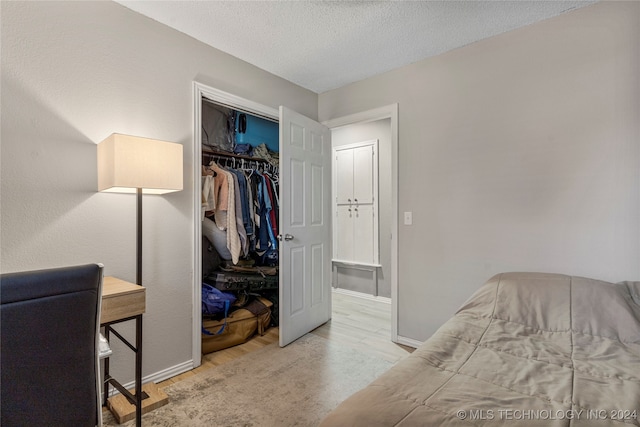 bedroom with light hardwood / wood-style floors, a textured ceiling, and a closet