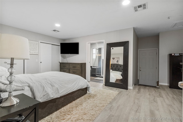 bedroom with black refrigerator, light wood-type flooring, ensuite bath, and a closet