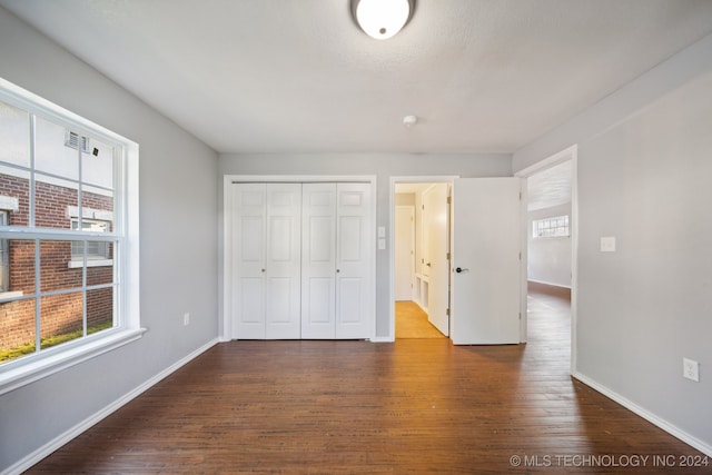 unfurnished bedroom featuring dark hardwood / wood-style floors, a closet, and multiple windows