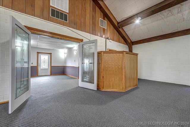 carpeted spare room with lofted ceiling with beams, wood walls, and french doors