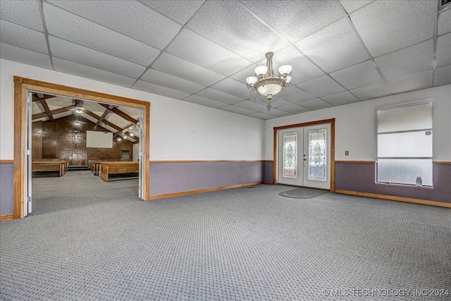 empty room featuring french doors, a drop ceiling, wood walls, vaulted ceiling, and ceiling fan with notable chandelier