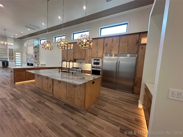 kitchen with pendant lighting, a towering ceiling, built in refrigerator, and a large island with sink