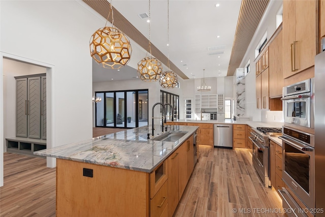 kitchen with light stone counters, a sink, stainless steel appliances, light wood-style floors, and a warming drawer