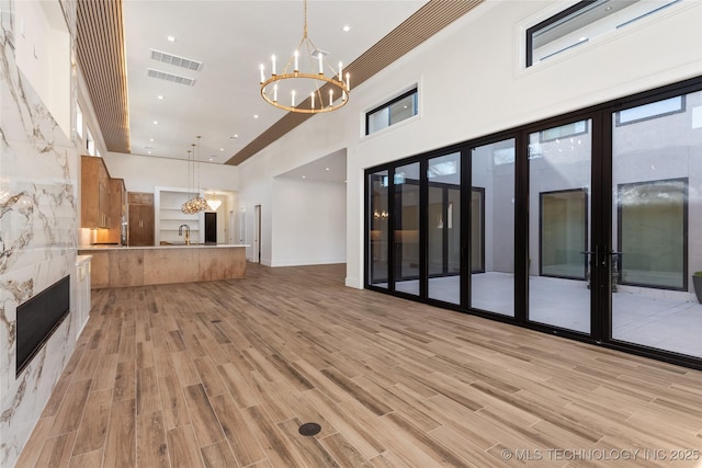 unfurnished living room featuring visible vents, a high ceiling, light wood-style floors, and an inviting chandelier