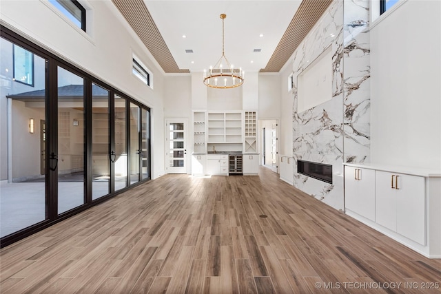 unfurnished living room featuring beverage cooler, a chandelier, light wood-style flooring, a fireplace, and a sink