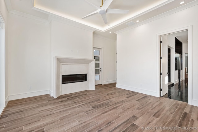 unfurnished living room featuring a glass covered fireplace, crown molding, a tray ceiling, and wood tiled floor