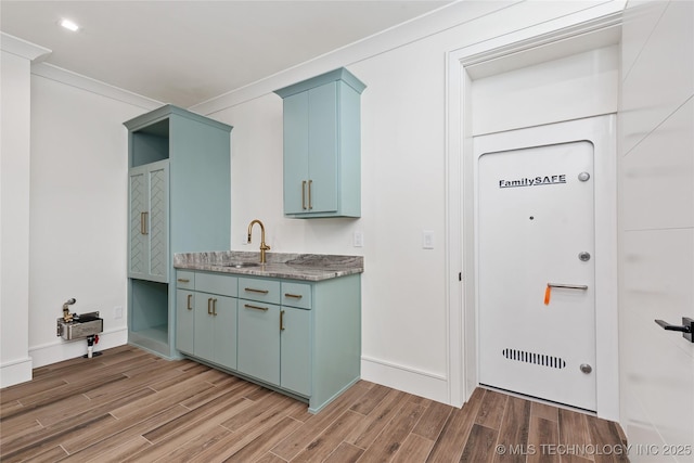 kitchen featuring light stone counters, ornamental molding, a sink, light wood-style floors, and blue cabinets