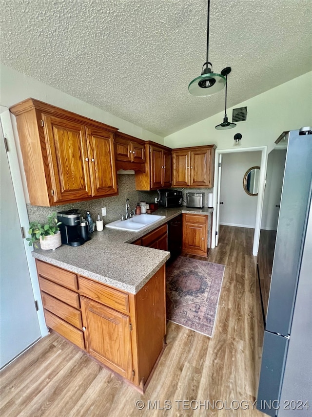 kitchen featuring sink, light hardwood / wood-style flooring, lofted ceiling, decorative light fixtures, and decorative backsplash