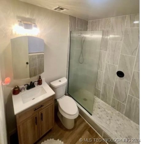 bathroom featuring a tile shower, vanity, hardwood / wood-style flooring, and toilet