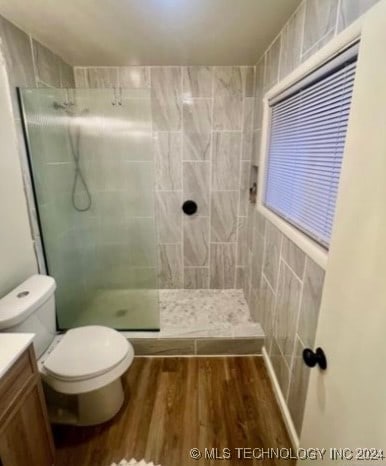 bathroom with wood-type flooring, toilet, tiled shower, vanity, and tile walls