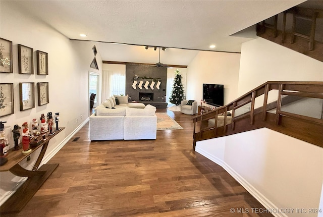 living room with ceiling fan, dark wood-type flooring, a brick fireplace, a textured ceiling, and vaulted ceiling