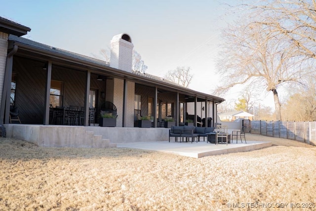 back of house with brick siding, a patio, a chimney, fence, and an outdoor living space