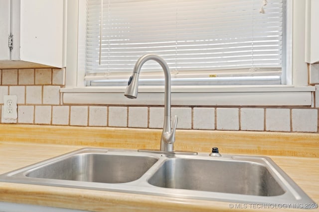 details with tasteful backsplash, white cabinetry, and sink