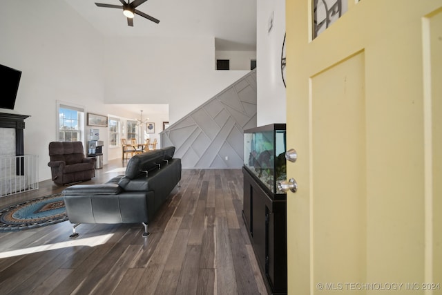 living room featuring dark hardwood / wood-style flooring, ceiling fan with notable chandelier, and a high ceiling