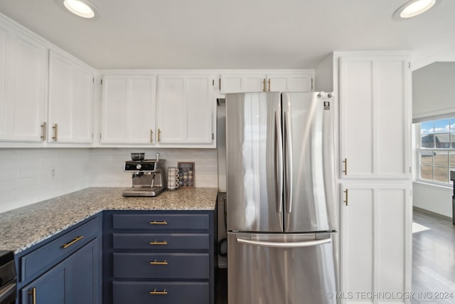 kitchen featuring decorative backsplash, stainless steel fridge, blue cabinetry, wood-type flooring, and white cabinets