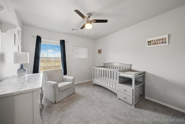 bedroom with ceiling fan, a crib, and light carpet