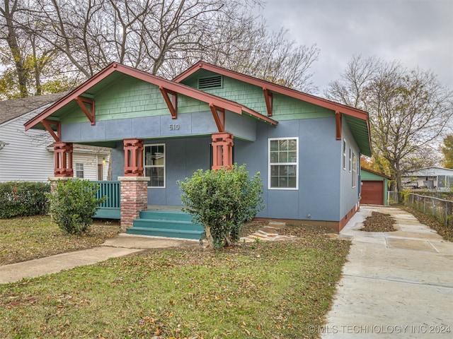 view of front of property with an outbuilding, covered porch, a front yard, and a garage