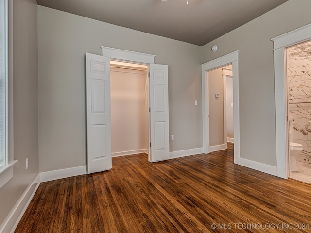 unfurnished bedroom with ensuite bathroom, a closet, and dark wood-type flooring