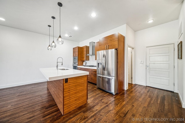 kitchen with sink, wall chimney exhaust hood, stainless steel appliances, decorative light fixtures, and a kitchen island with sink