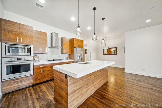 kitchen featuring a center island with sink, dark hardwood / wood-style floors, wall chimney range hood, and appliances with stainless steel finishes