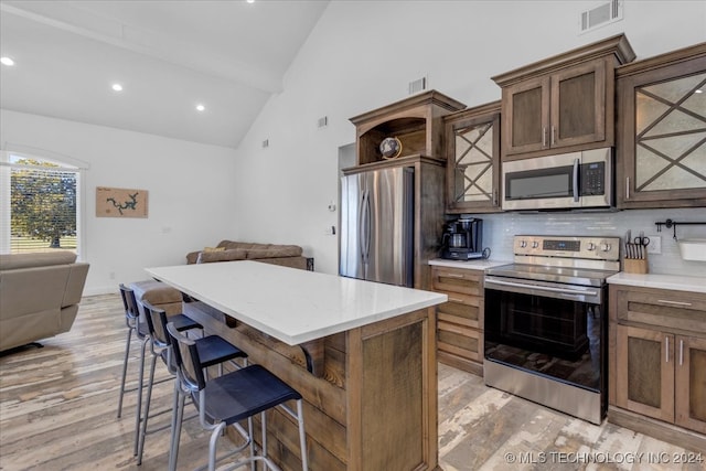 kitchen featuring a kitchen bar, backsplash, stainless steel appliances, and light wood-type flooring