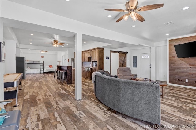 living room featuring hardwood / wood-style flooring, ceiling fan, a barn door, and wood walls