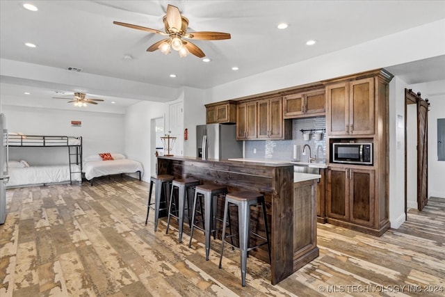 kitchen featuring a kitchen bar, appliances with stainless steel finishes, tasteful backsplash, a barn door, and light hardwood / wood-style floors