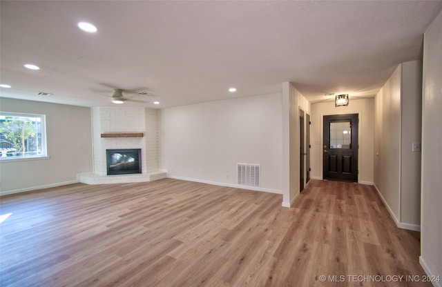 unfurnished living room with ceiling fan, light hardwood / wood-style floors, and a brick fireplace