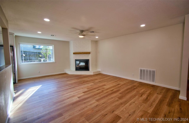 unfurnished living room featuring a brick fireplace, ceiling fan, and light wood-type flooring