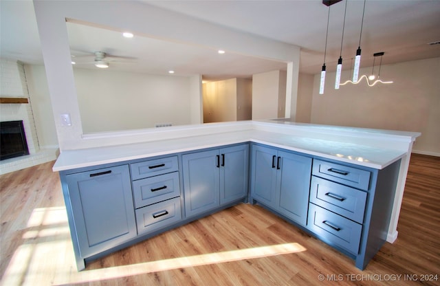 kitchen featuring ceiling fan, pendant lighting, light hardwood / wood-style floors, and a brick fireplace