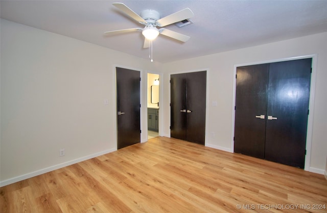 unfurnished bedroom featuring light wood-type flooring, ensuite bath, ceiling fan, and multiple closets