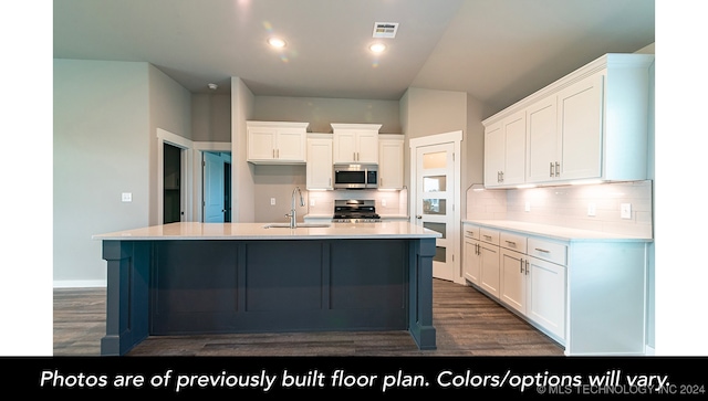 kitchen with dark wood-type flooring, stainless steel appliances, decorative backsplash, a center island with sink, and white cabinets