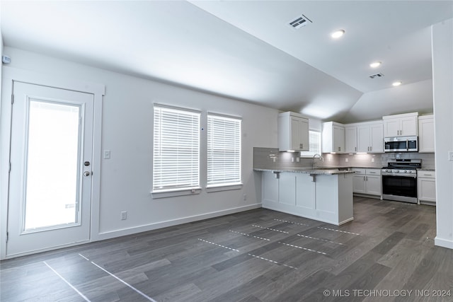 kitchen featuring dark hardwood / wood-style flooring, kitchen peninsula, lofted ceiling, white cabinets, and appliances with stainless steel finishes