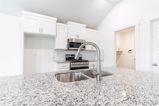 kitchen with stainless steel appliances, light stone counters, backsplash, vaulted ceiling, and white cabinets